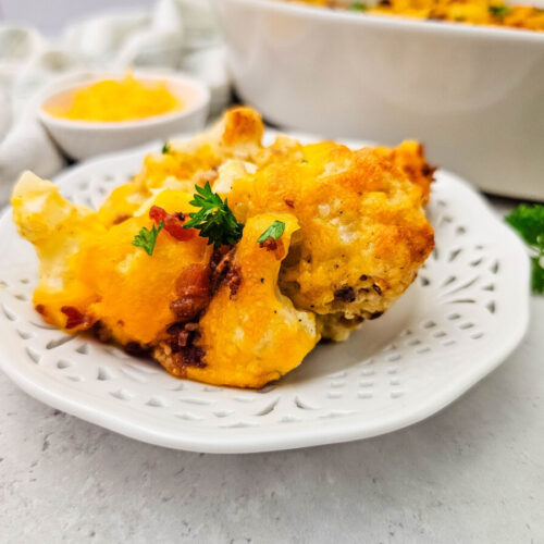 Baked cauliflower casserole with cheese topping, garnished with parsley, served on white plate with melted butter