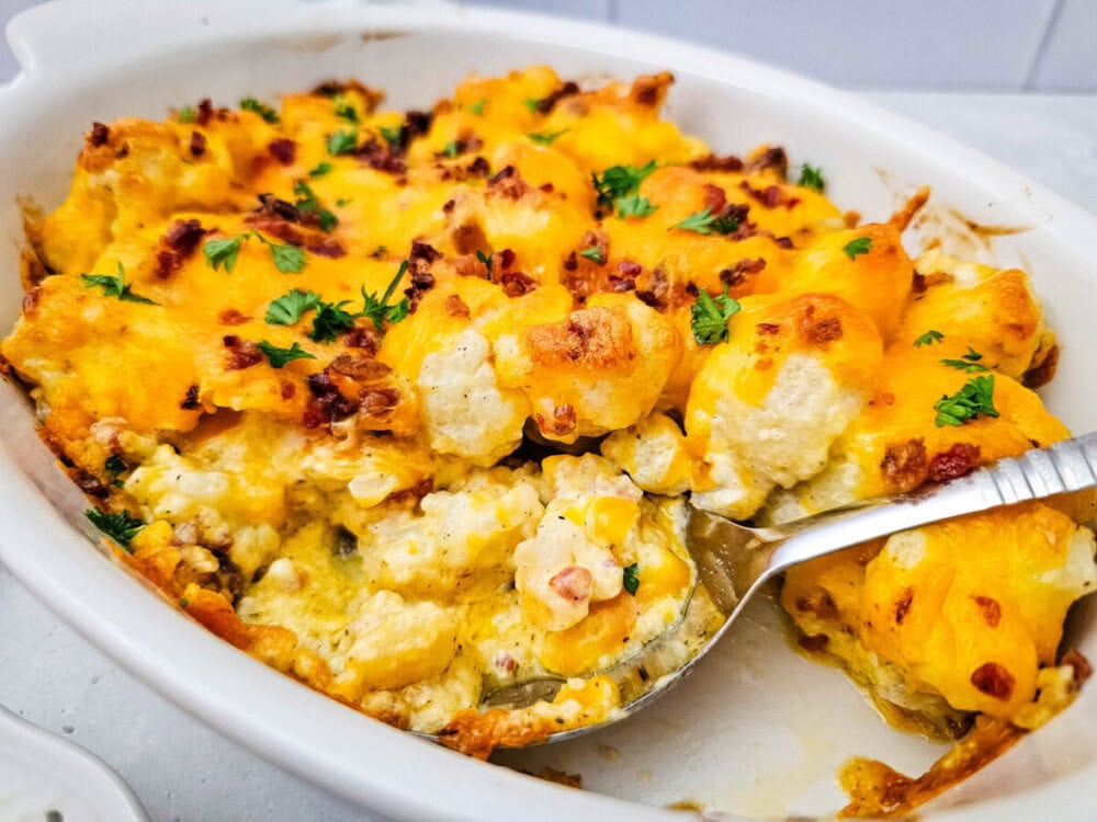 Baked cauliflower casserole with cheddar cheese, bacon, and parsley garnish in white dish