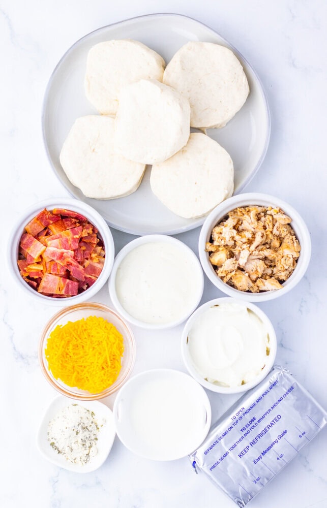 Ingredients for chicken bacon ranch bubble up bake arranged in bowls including biscuits, bacon, walnuts, cheese, sour cream, and seasonings