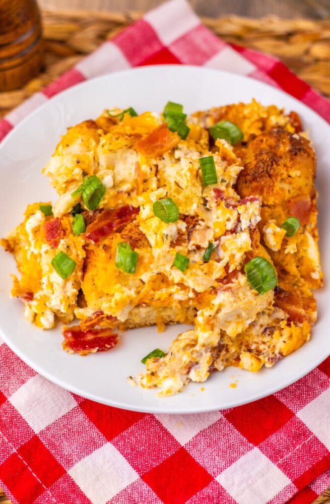 Chicken Bacon Ranch Bubble Up Bake casserole garnished with green onions and bacon on white plate with checkered cloth