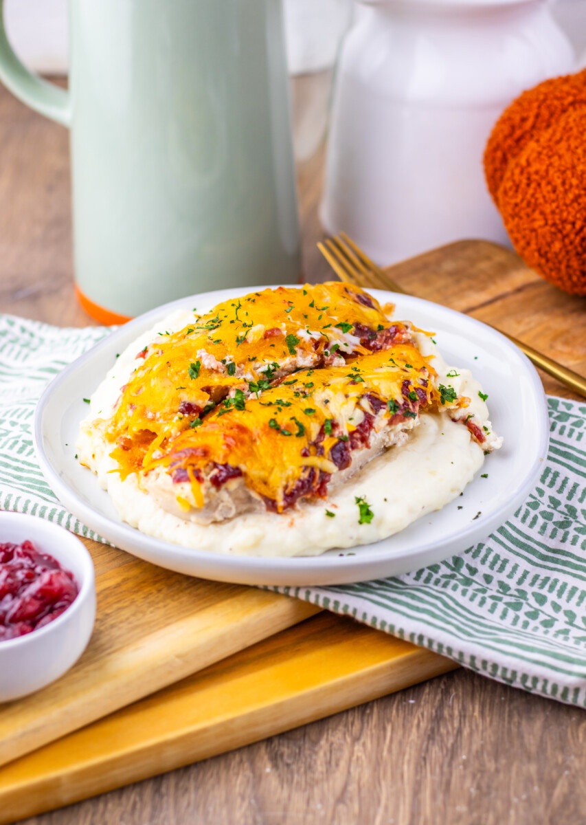 Cranberry Cream Cheese Chicken Bake with melted cheddar cheese and fresh herb garnish on white plate