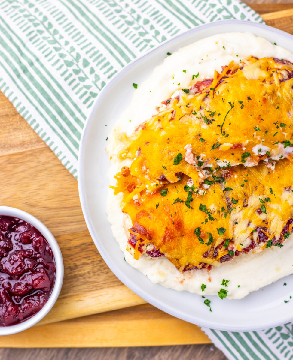 Cranberry cream cheese chicken bake with melted cheddar cheese and fresh parsley, served with cranberry sauce