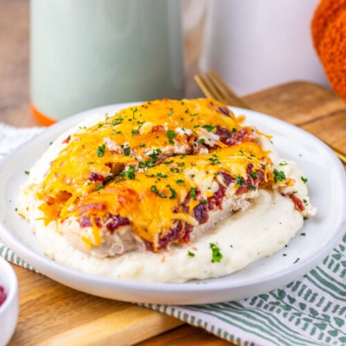 Cranberry Cream Cheese Chicken Bake plated on white dish with melted cheddar cheese, fresh herbs, and cranberry garnish