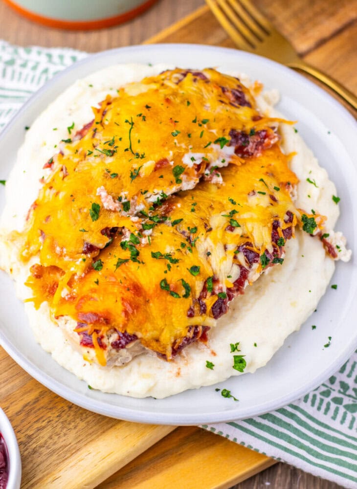 Cranberry cream cheese chicken bake topped with melted cheddar cheese and bacon garnish on white plate