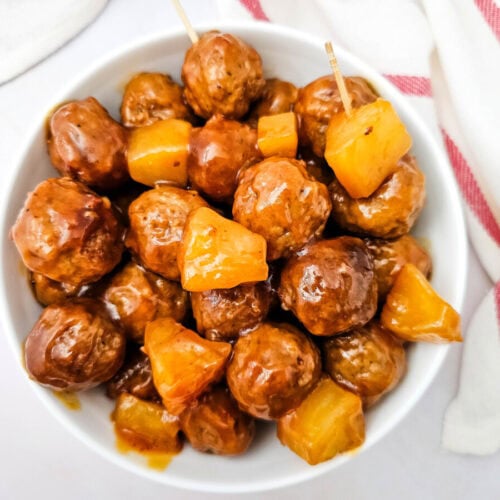Crockpot sweet and sour meatballs with pineapple chunks in white bowl, overhead view