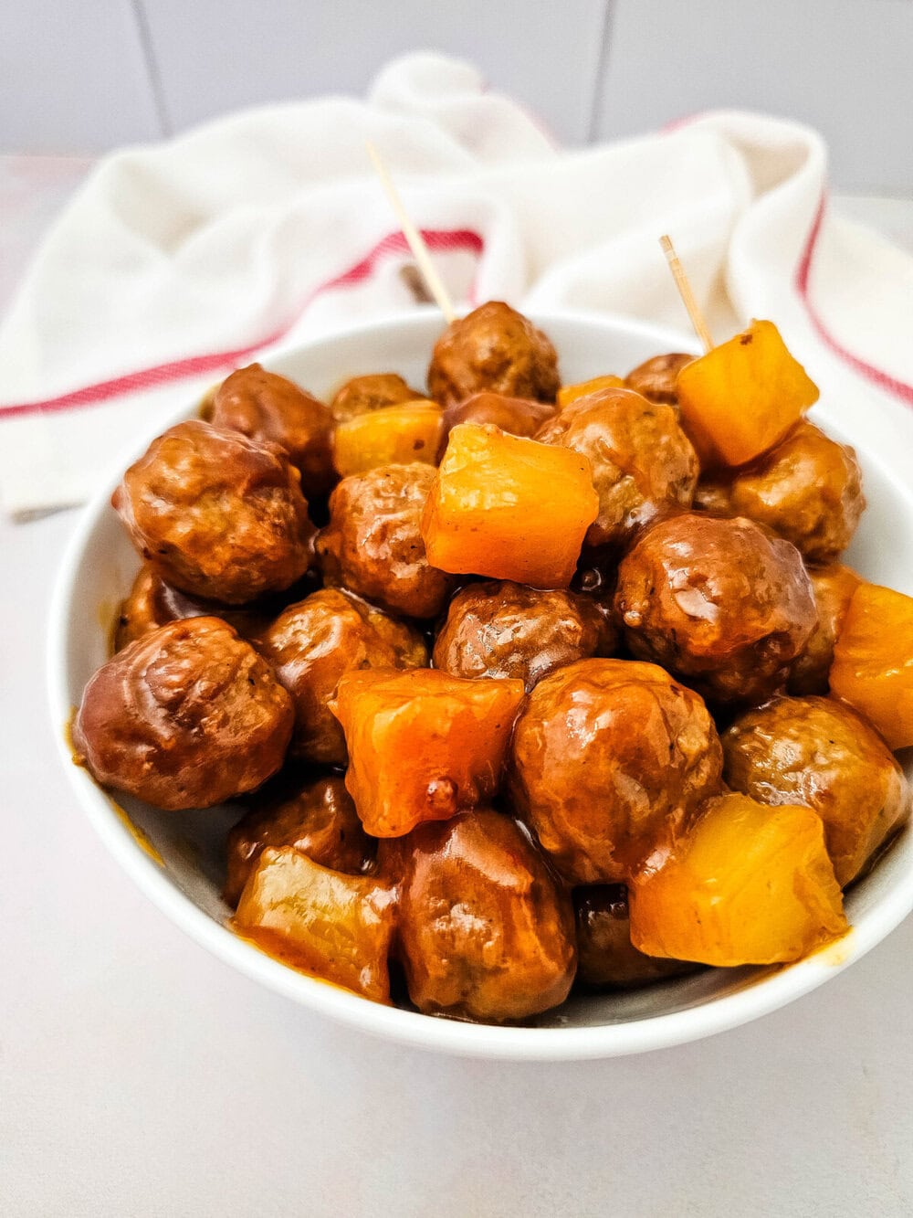 Crockpot sweet and sour meatballs with pineapple and peppers in white serving bowl