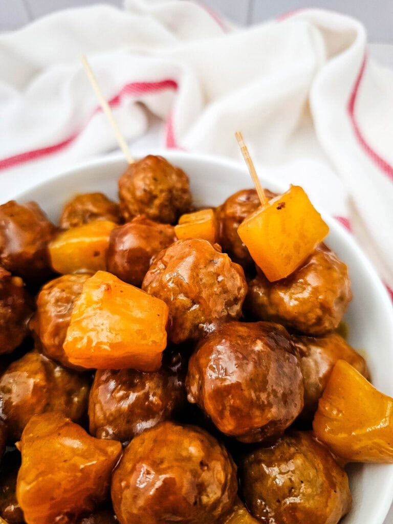 Crockpot sweet and sour meatballs with pineapple in white serving bowl