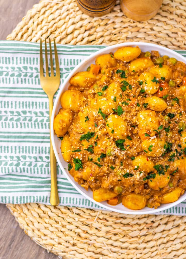 One Pan Gnocchi Shepherd's Pie with golden potato gnocchi, ground meat sauce, and fresh parsley on white plate