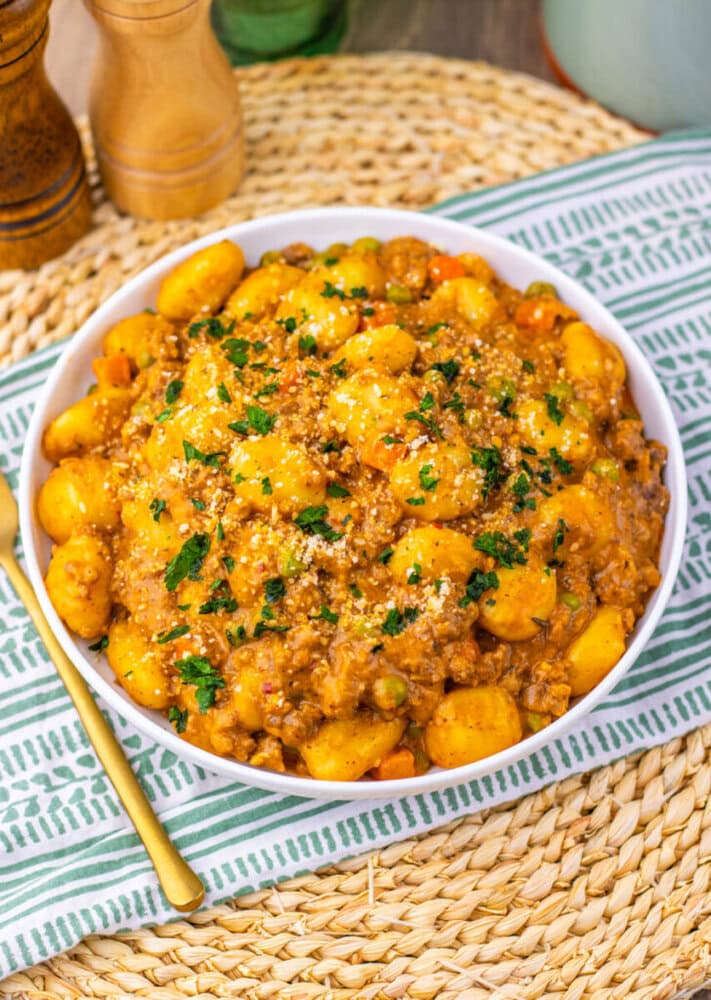 One Pan Gnocchi Shepherd's Pie with golden potato gnocchi, meat sauce, and parsley garnish in white bowl
