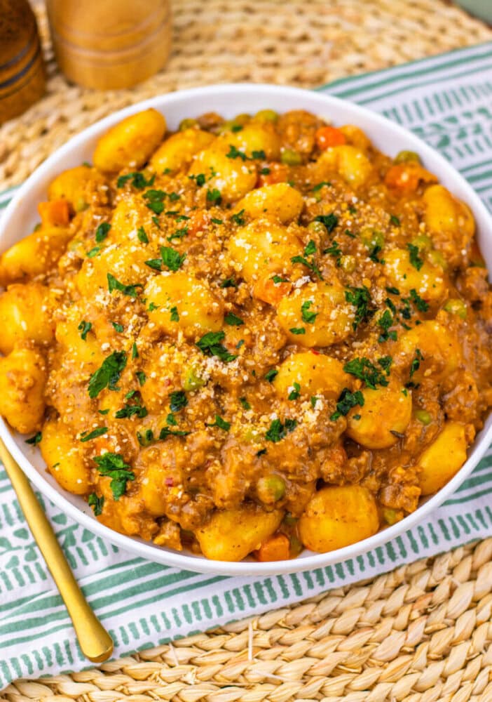 One Pan Gnocchi Shepherd's Pie with golden gnocchi, meat sauce, and parsley garnish in white bowl