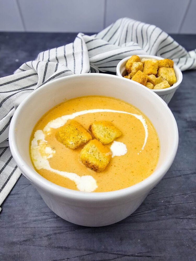 Creamy pumpkin soup in white bowl topped with golden croutons and cream swirl, ready to serve
