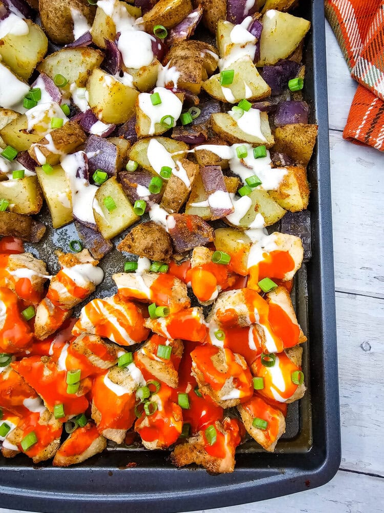 Sheet pan buffalo chicken with roasted red peppers, potatoes, and purple onions topped with sour cream and chives