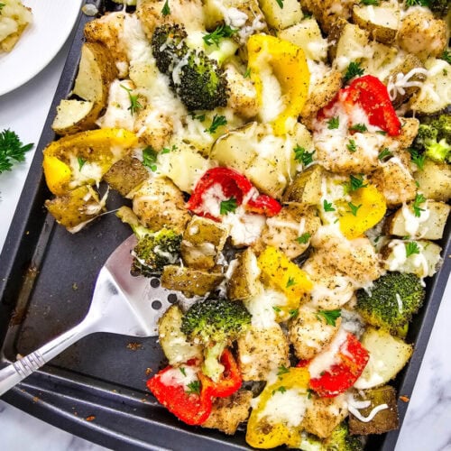 Sheet pan mozzarella chicken with roasted broccoli, red and yellow bell peppers, potatoes, and melted mozzarella cheese garnished with fresh parsley