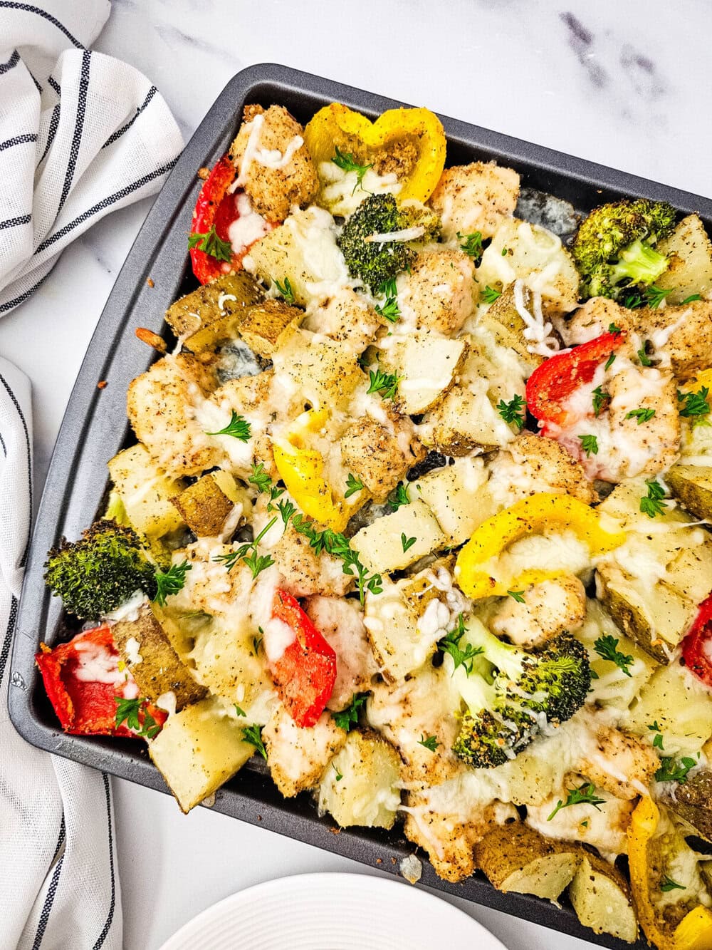 Sheet pan mozzarella chicken with roasted broccoli, bell peppers, and potatoes topped with melted cheese