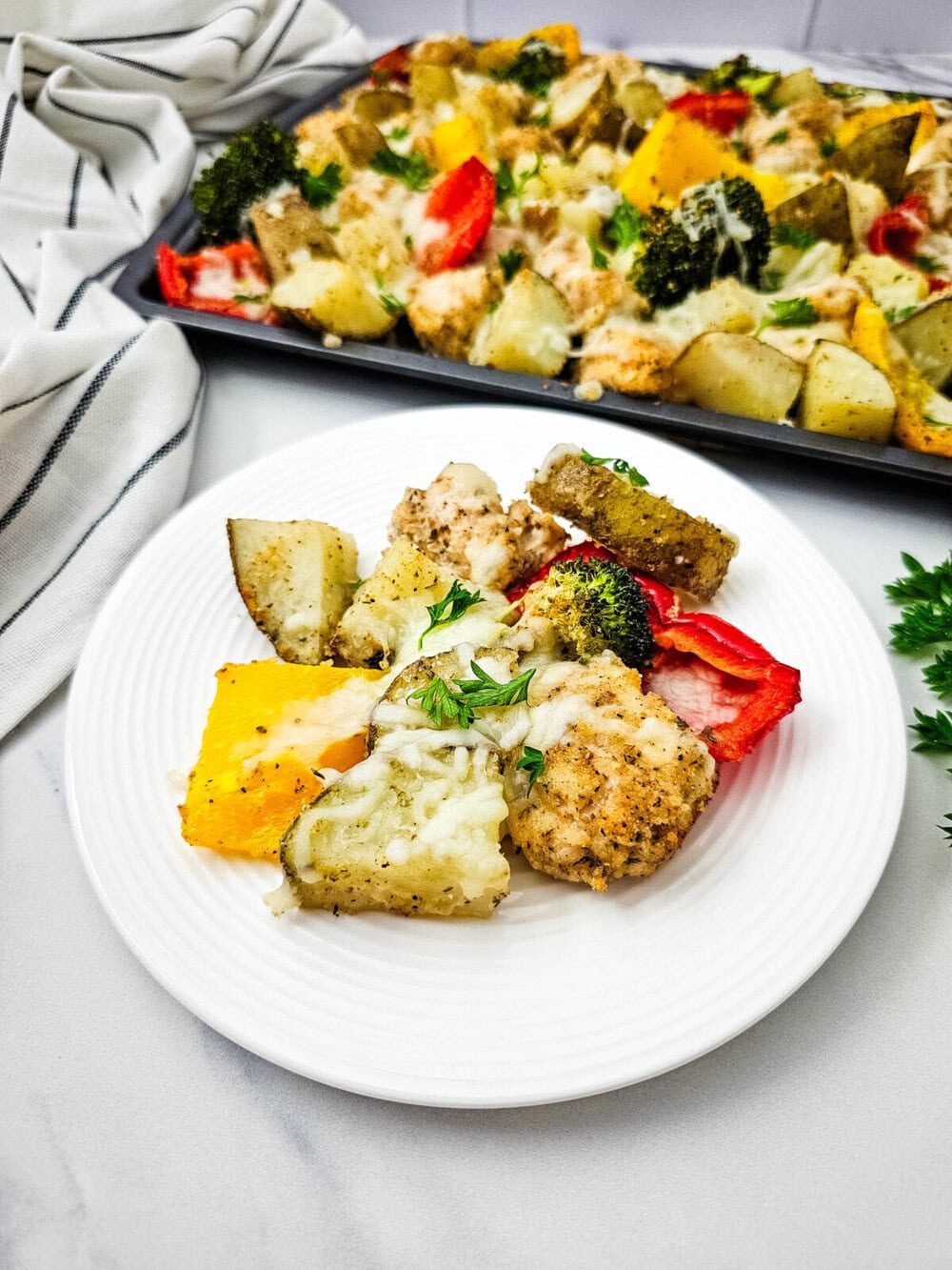 Sheet pan mozzarella chicken with roasted vegetables and melted cheese, plated on white dish