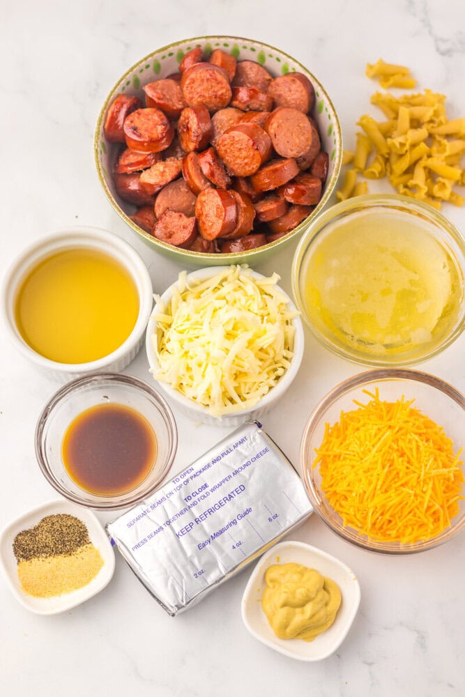 Slow cooker beer cheese sausage pasta ingredients laid out in bowls including sliced sausage, shredded cheese, beer, oil, mustard and seasonings