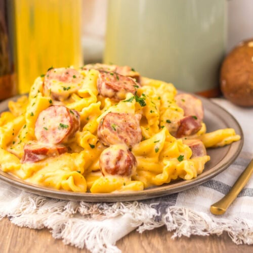 Slow cooker beer cheese sausage pasta plated with spiral noodles, sliced sausage, and parsley garnish