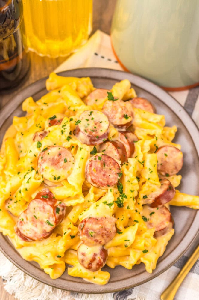 Slow cooker beer cheese sausage pasta with sliced sausage and fresh parsley garnish served on a plate