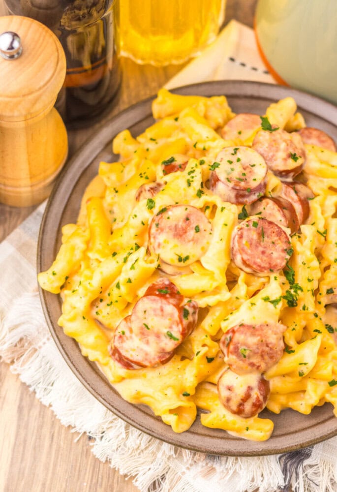 Slow cooker beer cheese sausage pasta with sliced sausage and fresh herbs on a plate