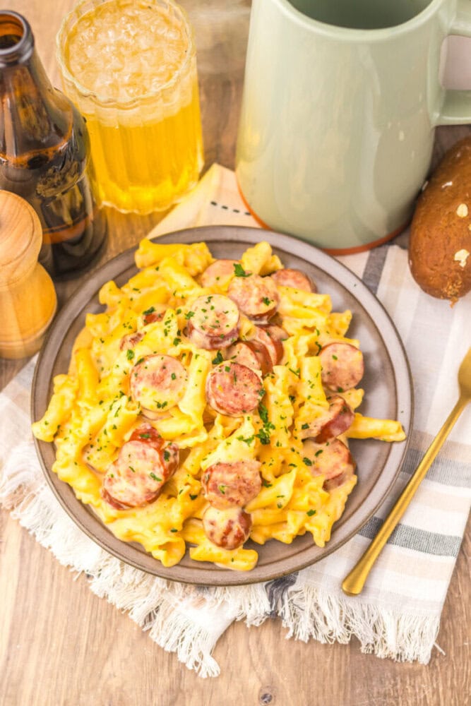 Slow cooker beer cheese sausage pasta with sliced sausage and fresh parsley garnish on a plate