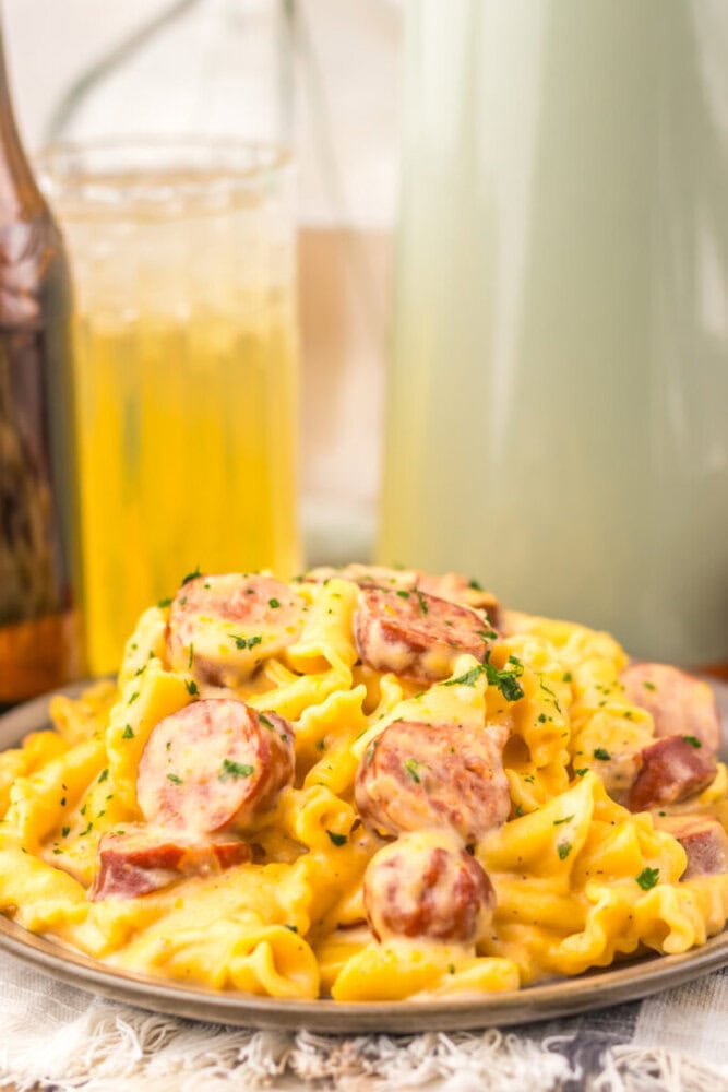 Slow cooker beer cheese sausage pasta with sliced kielbasa on rotini noodles garnished with parsley, served with beer