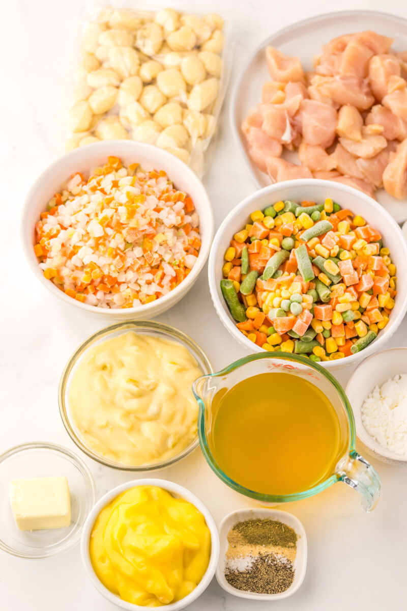 Slow cooker chicken pot pie gnocchi ingredients laid out in bowls including chicken, beans, vegetables, and condiments ready for cooking