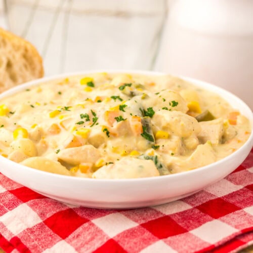 Slow cooker chicken pot pie gnocchi in white bowl with corn and parsley garnish on checkered cloth
