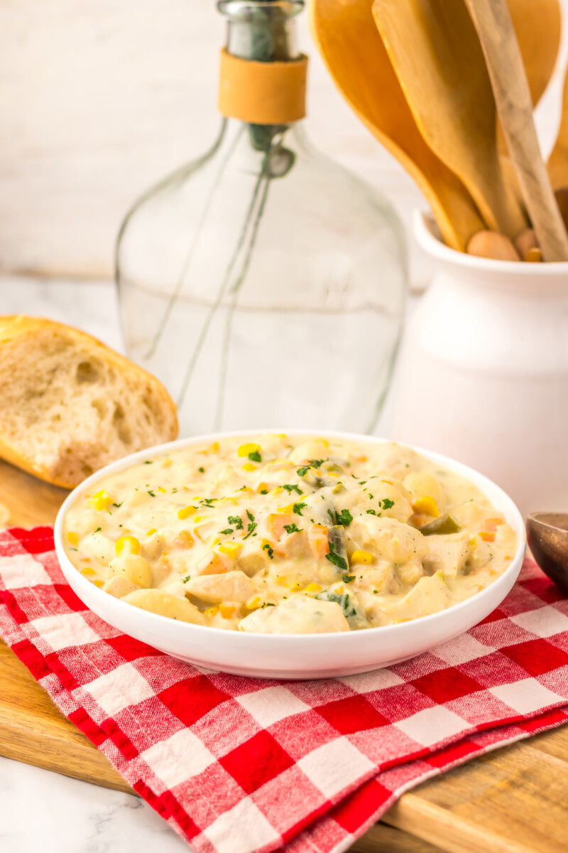 Creamy slow cooker chicken pot pie gnocchi in white bowl with herb garnish, served with crusty bread and wine