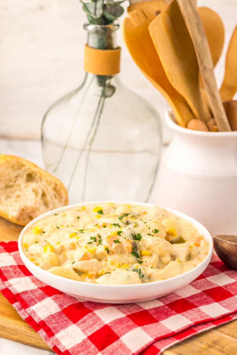 Slow cooker chicken pot pie gnocchi in white bowl with corn and herbs garnish, served with bread
