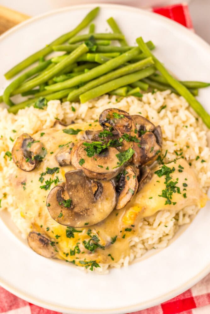 Slow cooker chicken and rice with mushroom sauce, green beans, and parsley garnish on white plate