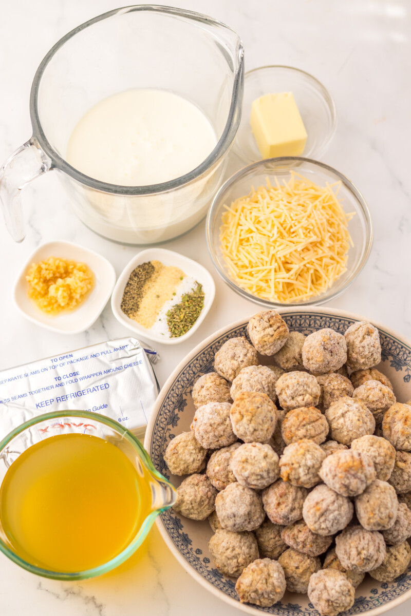 Slow cooker creamy alfredo meatballs ingredients including cooked meatballs, heavy cream, shredded cheese, butter, and seasonings laid out before cooking