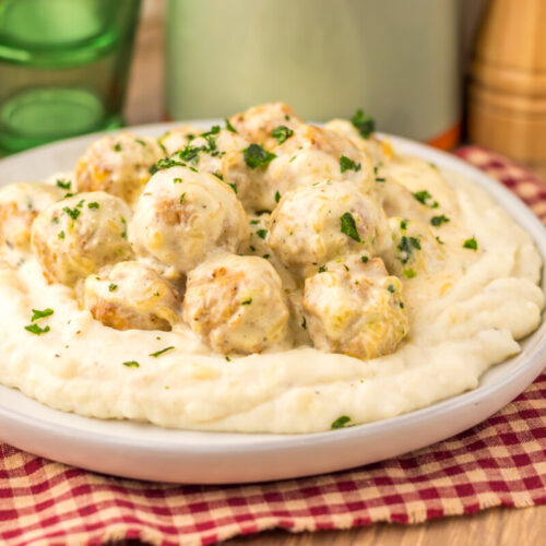 Slow cooker creamy alfredo meatballs served on mashed potato base with fresh parsley garnish