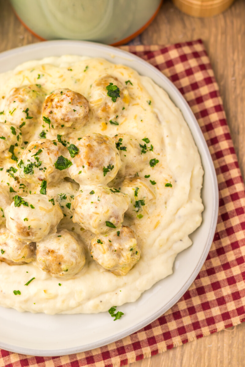 Slow cooker creamy alfredo meatballs served over mashed potatoes with fresh parsley garnish