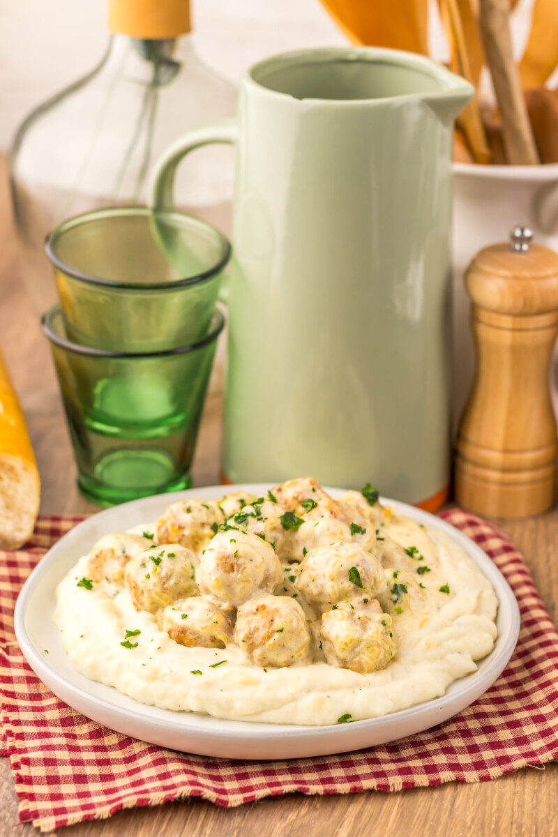 Slow cooker creamy alfredo meatballs served over mashed potatoes garnished with parsley
