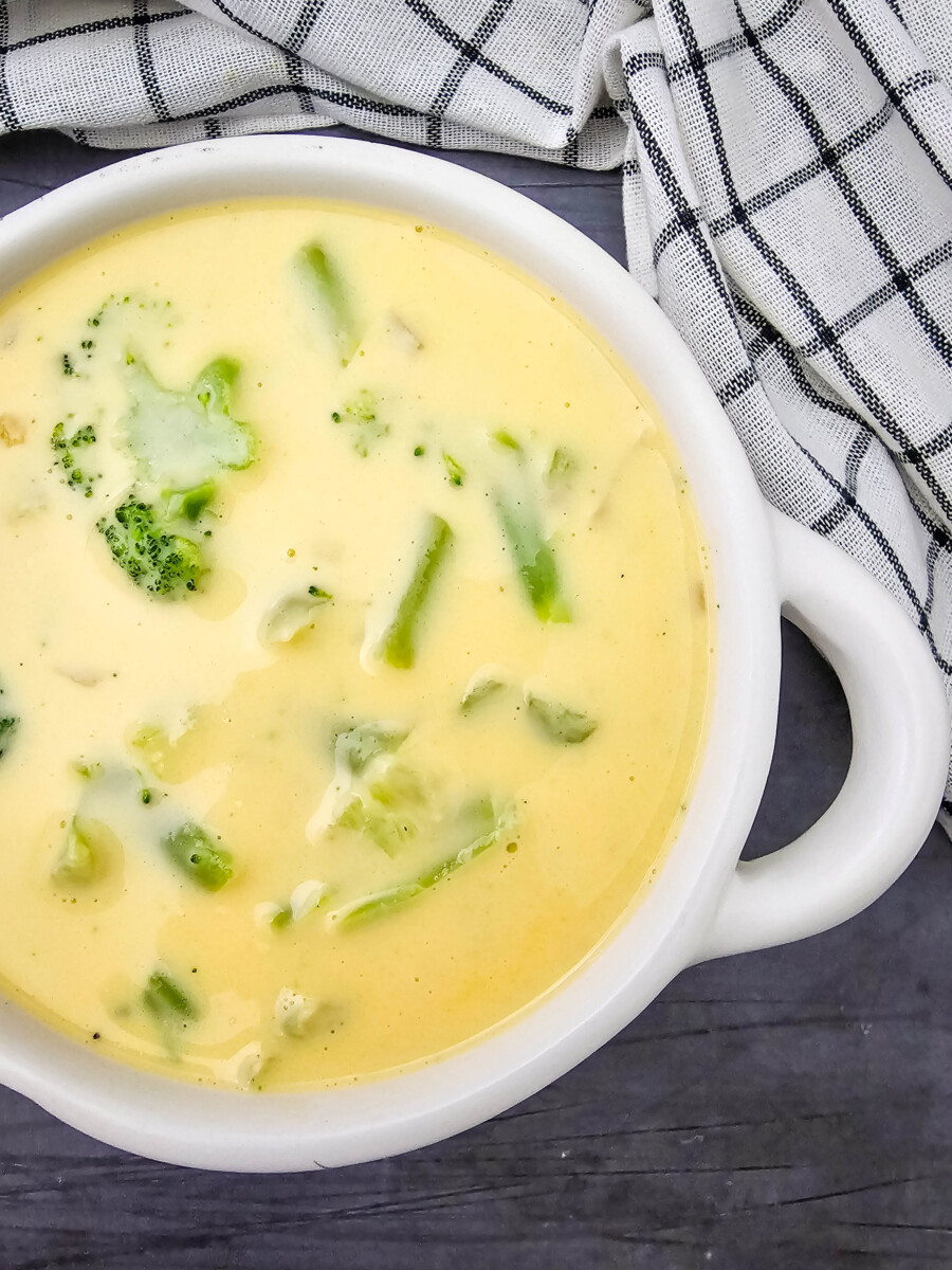 Creamy Velveeta broccoli cheese soup in white bowl with broccoli pieces and seasoning