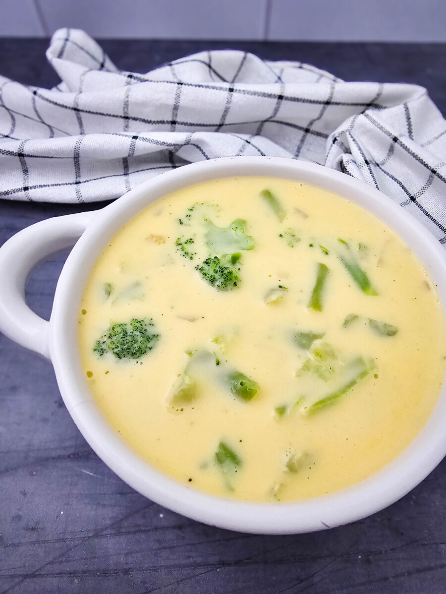 Velveeta cheese broccoli soup in white bowl with broccoli pieces and pepper garnish
