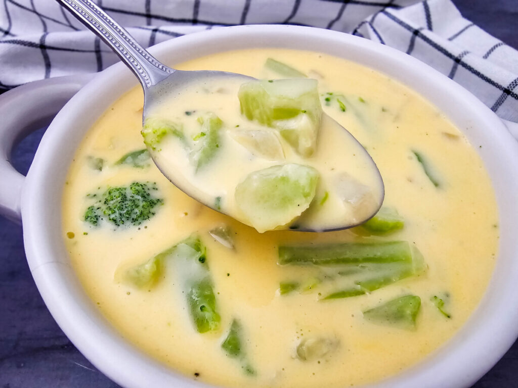 Creamy Velveeta broccoli cheese soup in white bowl with spoon and broccoli garnish