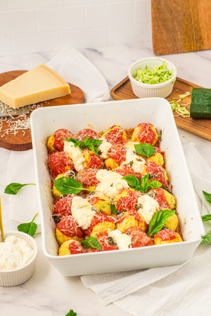 Baked chicken ricotta meatballs in tomato sauce with melted cheese and fresh basil in white baking dish