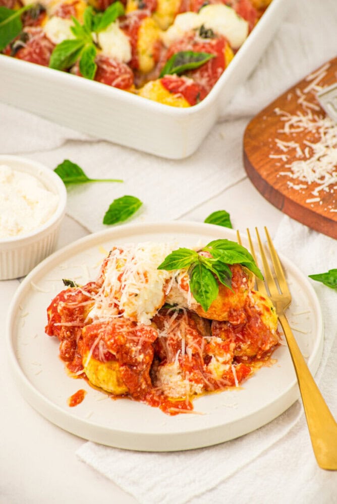 Chicken ricotta meatballs in tomato sauce topped with melted cheese and fresh basil on a white plate with gold fork