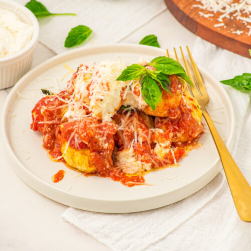 Chicken ricotta meatballs with marinara sauce and melted cheese on white plate garnished with fresh basil