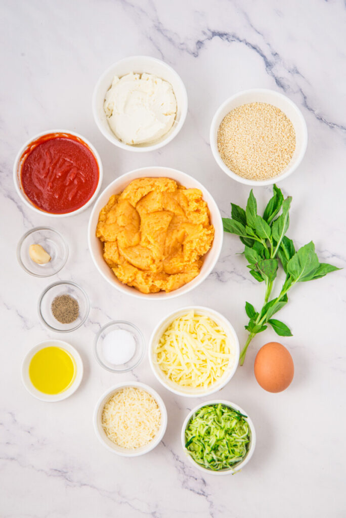 Chicken ricotta meatball ingredients laid out on marble countertop including cooked chicken, ricotta cheese, breadcrumbs, and fresh basil