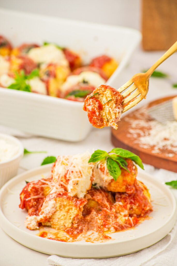 Chicken ricotta meatball on fork with melted cheese and tomato sauce, plated and ready to serve