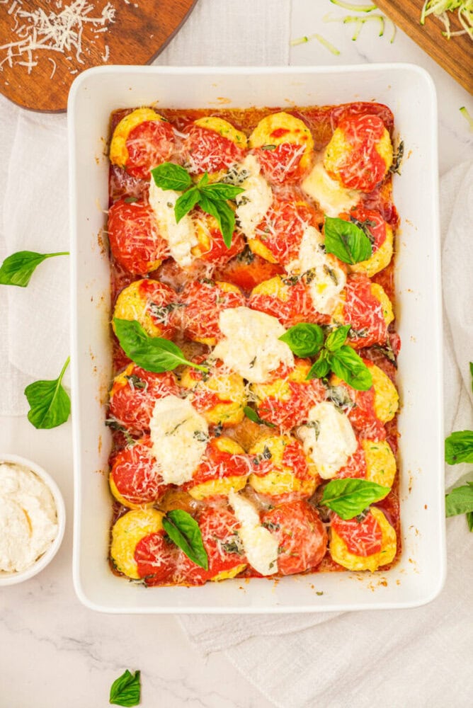 Baked tomato mozzarella casserole with fresh basil garnish in white dish