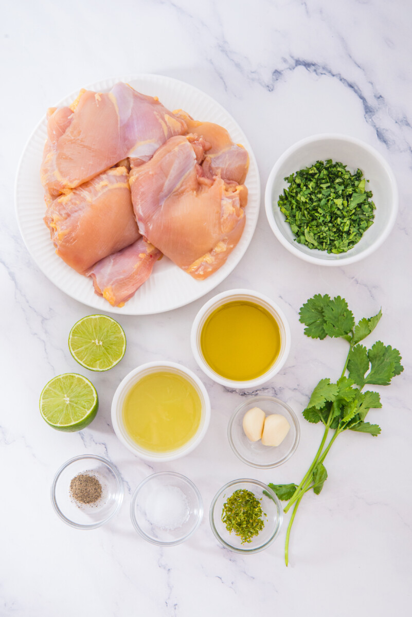 Cilantro lime chicken ingredients laid out flat including raw chicken breasts, fresh cilantro, lime, garlic, olive oil, and seasonings on marble