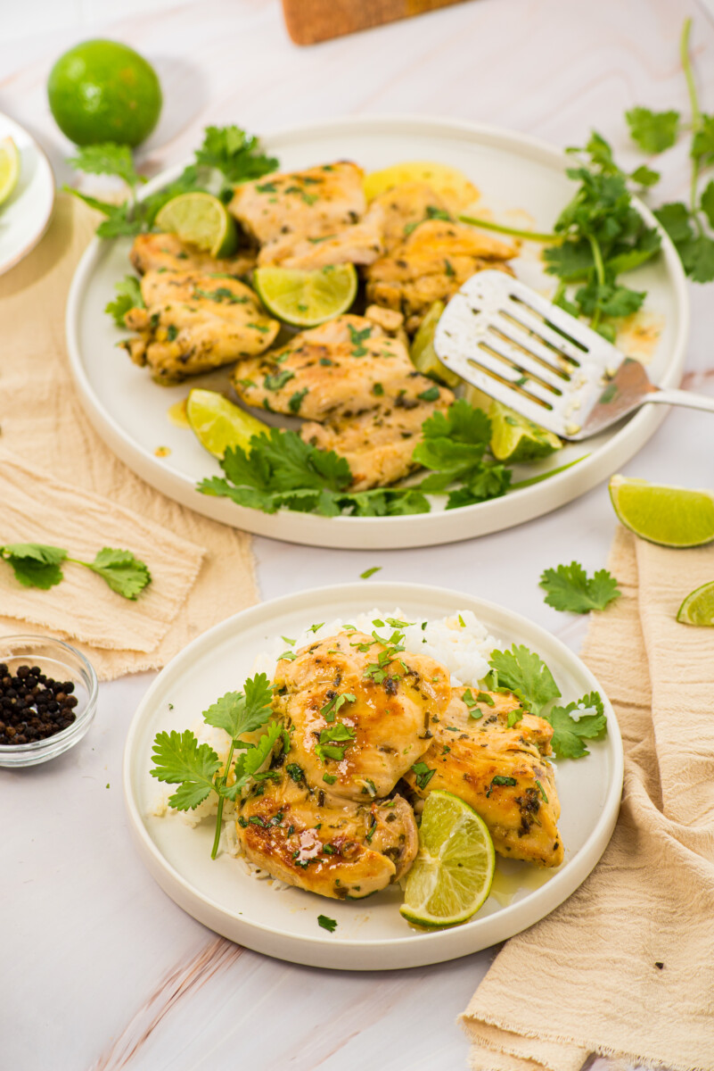 Cilantro lime chicken plated on white dishes garnished with fresh cilantro and lime wedges