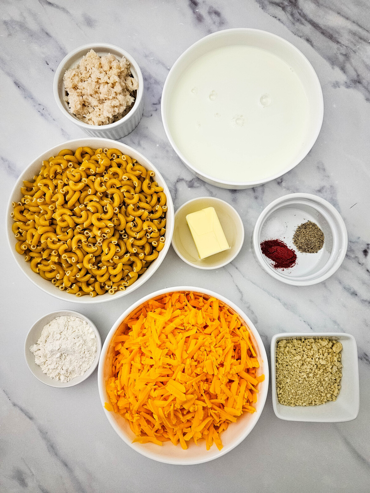 Crab mac and cheese ingredients laid out before cooking - pasta, cheese, cream, butter, and seasonings on marble counter