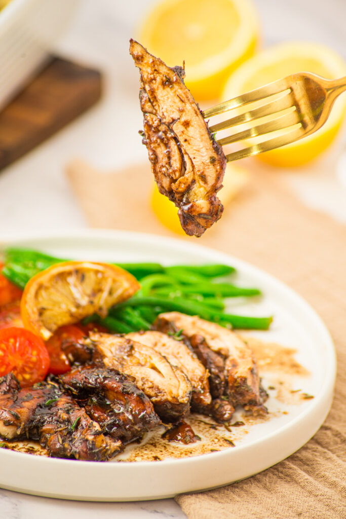 Honey balsamic chicken thighs plated with green beans and roasted vegetables, fork lifting caramelized chicken piece