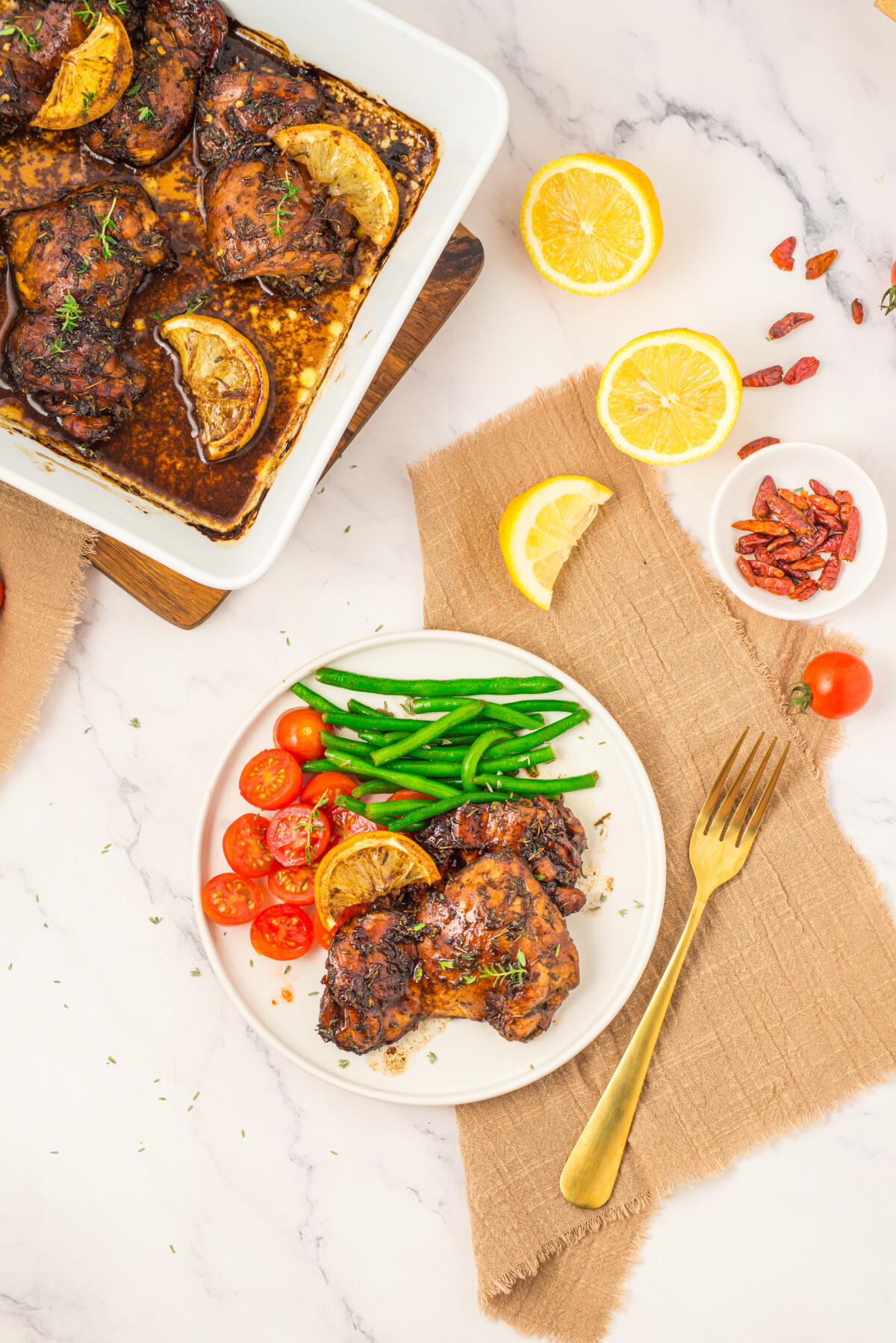 Honey balsamic chicken thighs plated with green beans and tomatoes, garnished with lemon slices