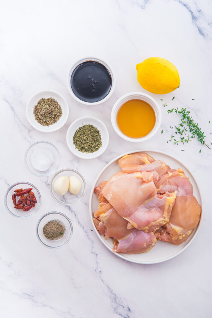 Honey balsamic chicken thighs ingredients laid out on marble countertop with raw chicken thighs, lemon, and seasonings
