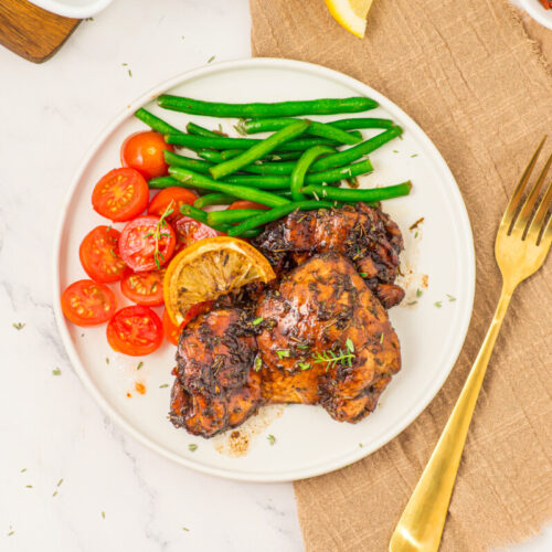 Honey balsamic chicken thighs plated with green beans and tomatoes, overhead shot